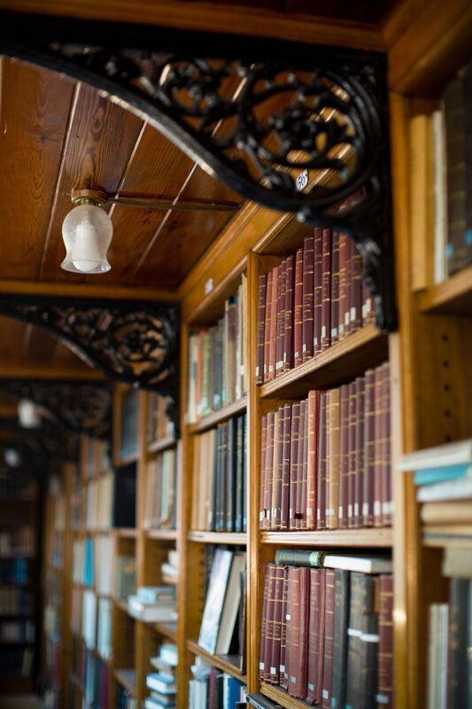 A close up of bookshelves in the Linnean Society library. There are brackets with floral details and a tulip shaped lamp overhead.