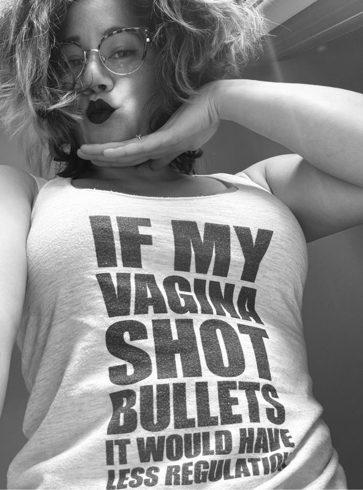 black and white photo of joa, a half korean woman with cateye glasses and black lipstick, kissing down at you and wearing a tank that says if my vagina shot bullets it would have less regulation