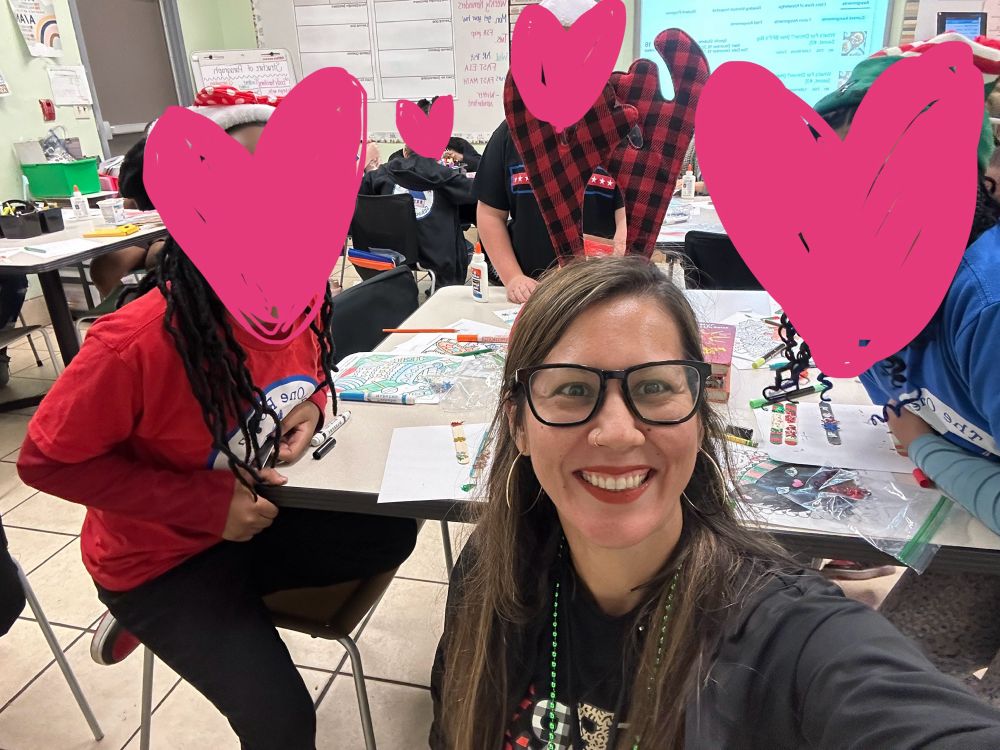 a selfie of my sister and some of her students but all of their faces are blocked out by pink hearts

she is a half korean woman with black glasses, red lipstick, gold hoop earrings and a big smile 