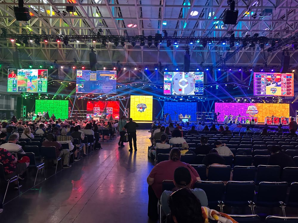 A view of all 4 competition stages at the Pokemon North America international championships. They are bright and colorful, and rows and rows of seats and spectators are visible. 