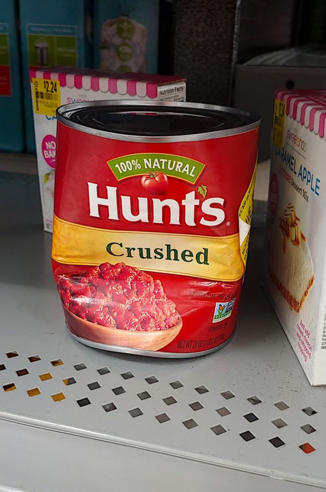 A can of Hunt's Crushed Tomatoes at the grocery store. The can is literally crushed!