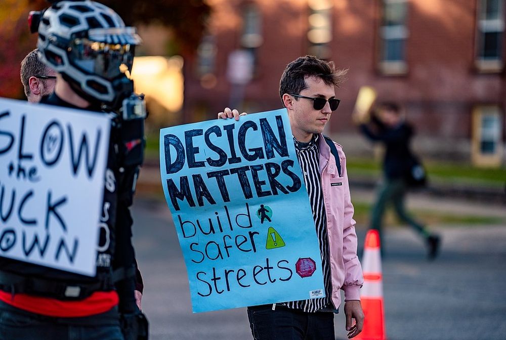 Photo of a man holding a sign saying "Design Matters Build Safer Streets.