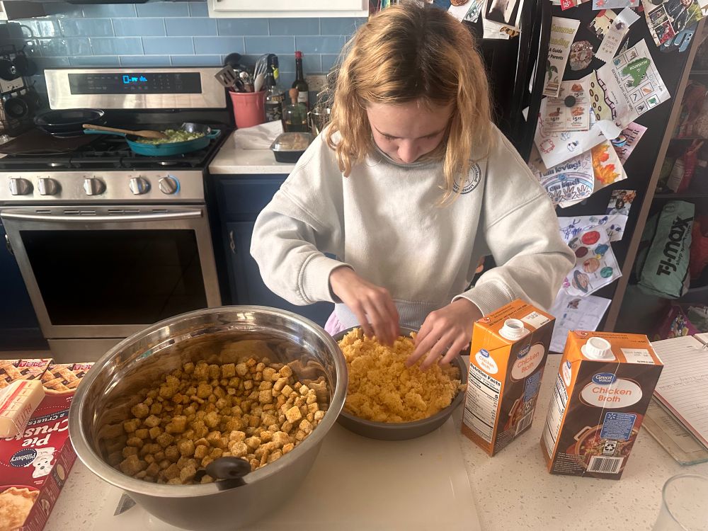 Granddaughter crumbling the cornbread to put into the dressing. Onions & celery sautéing on stove 