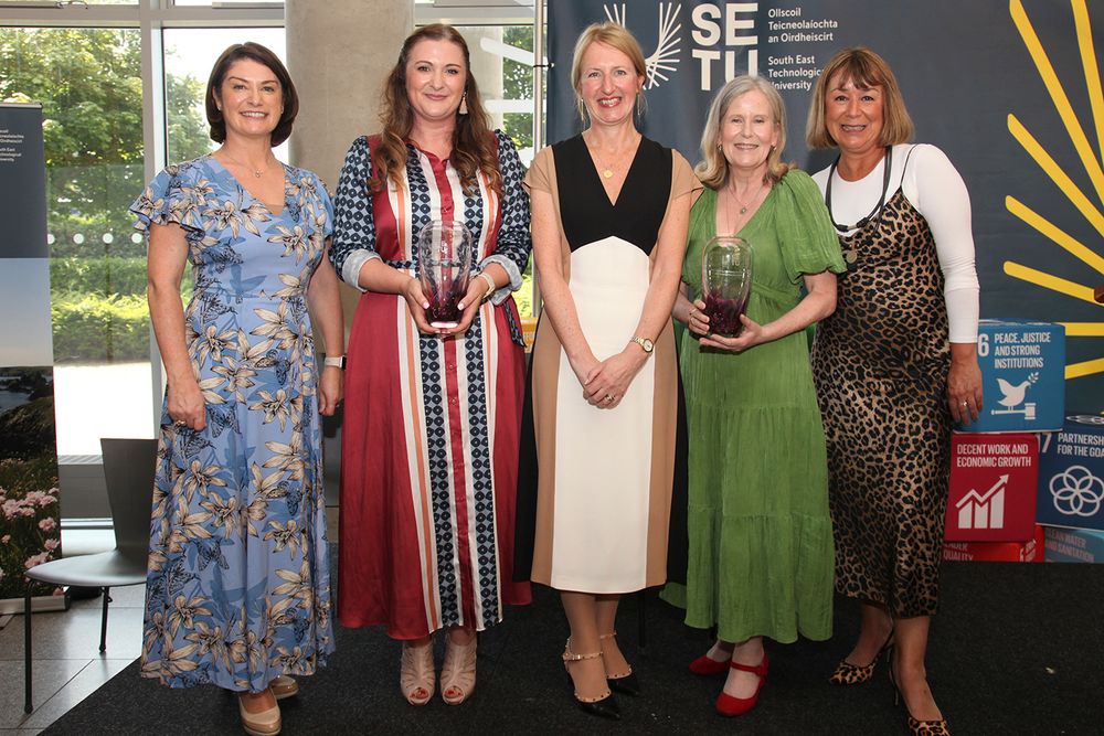 Five people pose for photo, two holding glass vases.