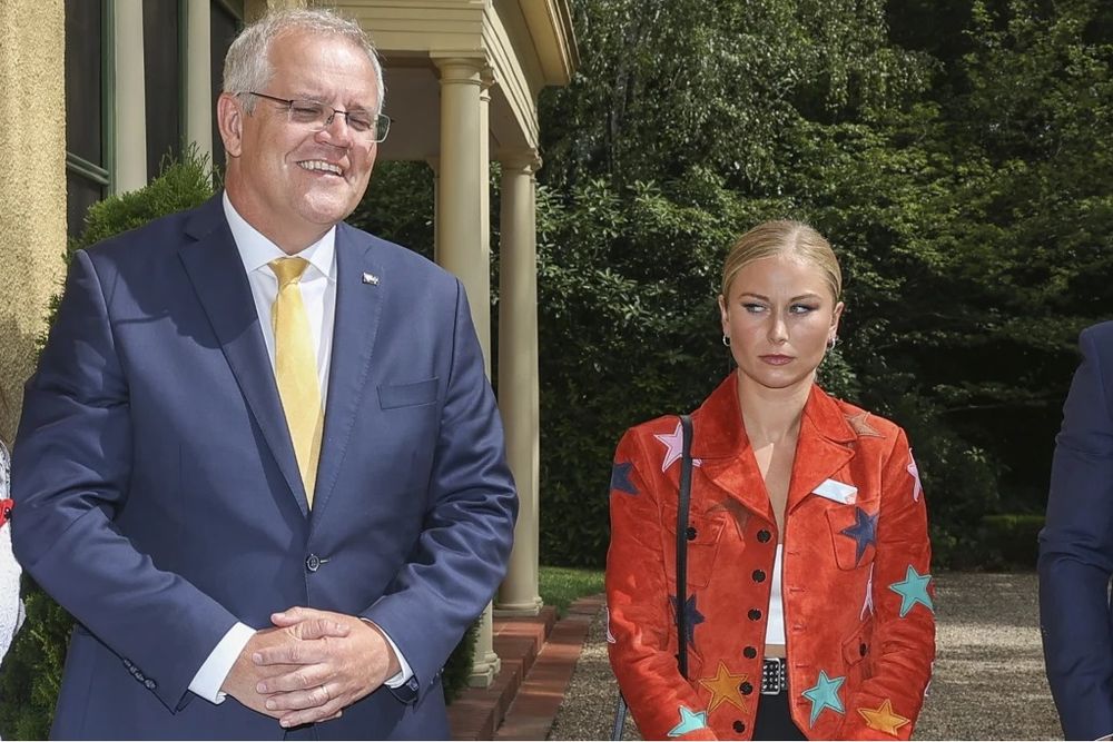 Grace Tame, advocate for victims of sexual violence, stands to the side of then Prime Minister, Scott Morrison. Scott Morrison smiles at the camera, while Grace Tame looks at him out of the corner of her eyes. This the famous Grace Tame 'side eye' incident.