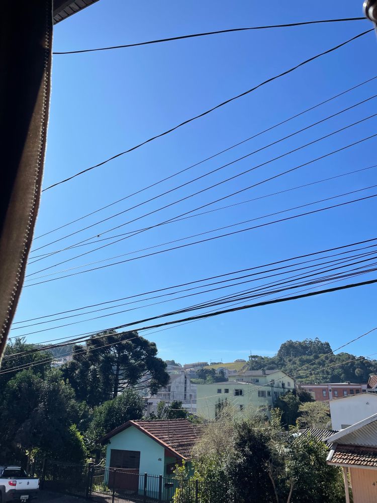 Foto da janela mostrando o céu azul e a paisagem urbana de uma pequena cidade da serra gaúcha com casas, prédios e árvores