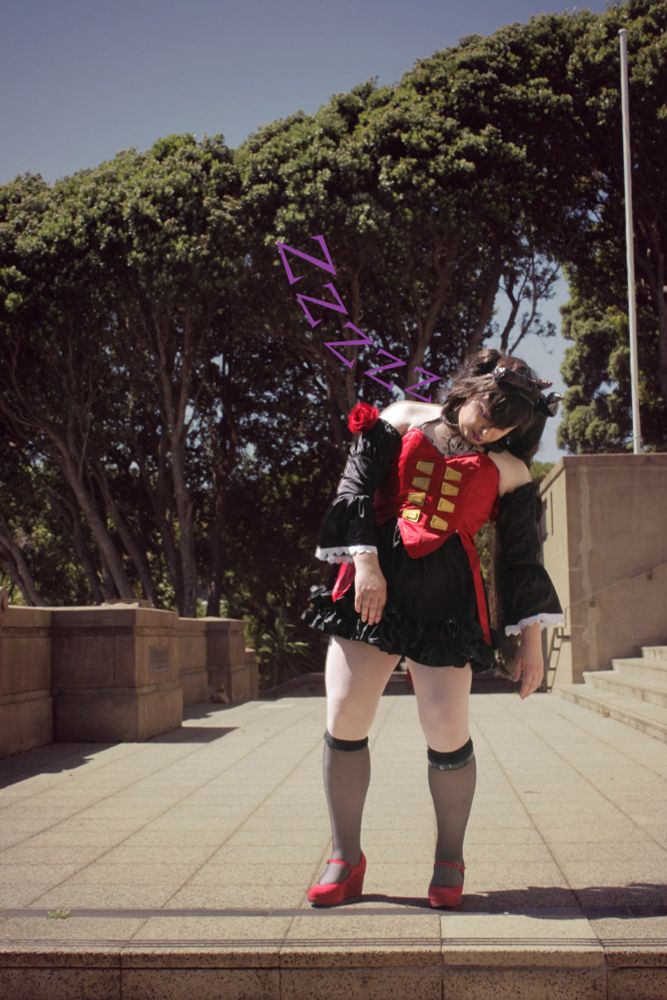 A picture of Charlotte cosplaying Eliza from Tekken 8, with a red bodice, devil horns and purple makeup falling asleep while standing up