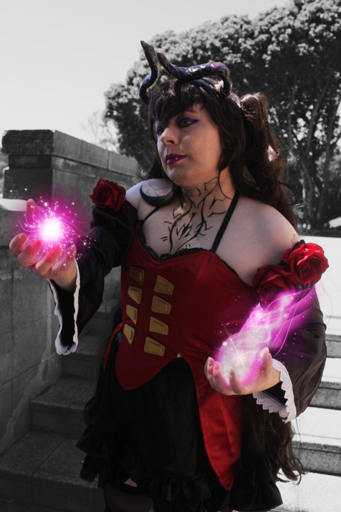 A picture of Charlotte cosplaying Eliza from Tekken 8, with a red bodice, devil horns and purple makeup with purple energy radiating from her hands