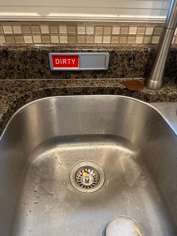 An empty sink with a “clean/dirty” indicator sign just behind it.