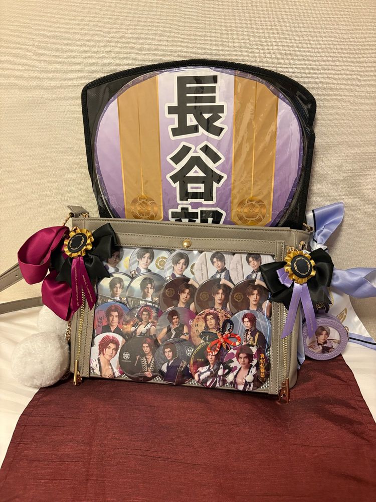 Uchiwa with Hasebe colors behind an ita bag sporting Hasebe and Tonbokiri ribbons, half Tonbokiri and half Hasebe badges. There are also Hasebe can badge holder and Muramasa souki pom pom keychains.