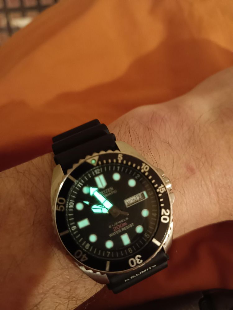 A citizen promaster automatic, hands glowing green on arm resting on orange bedsheet