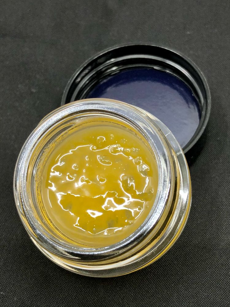 Cannabis live resin. Yellow translucent chunky apple sauce consistency extract. In a clear jar. Black background 