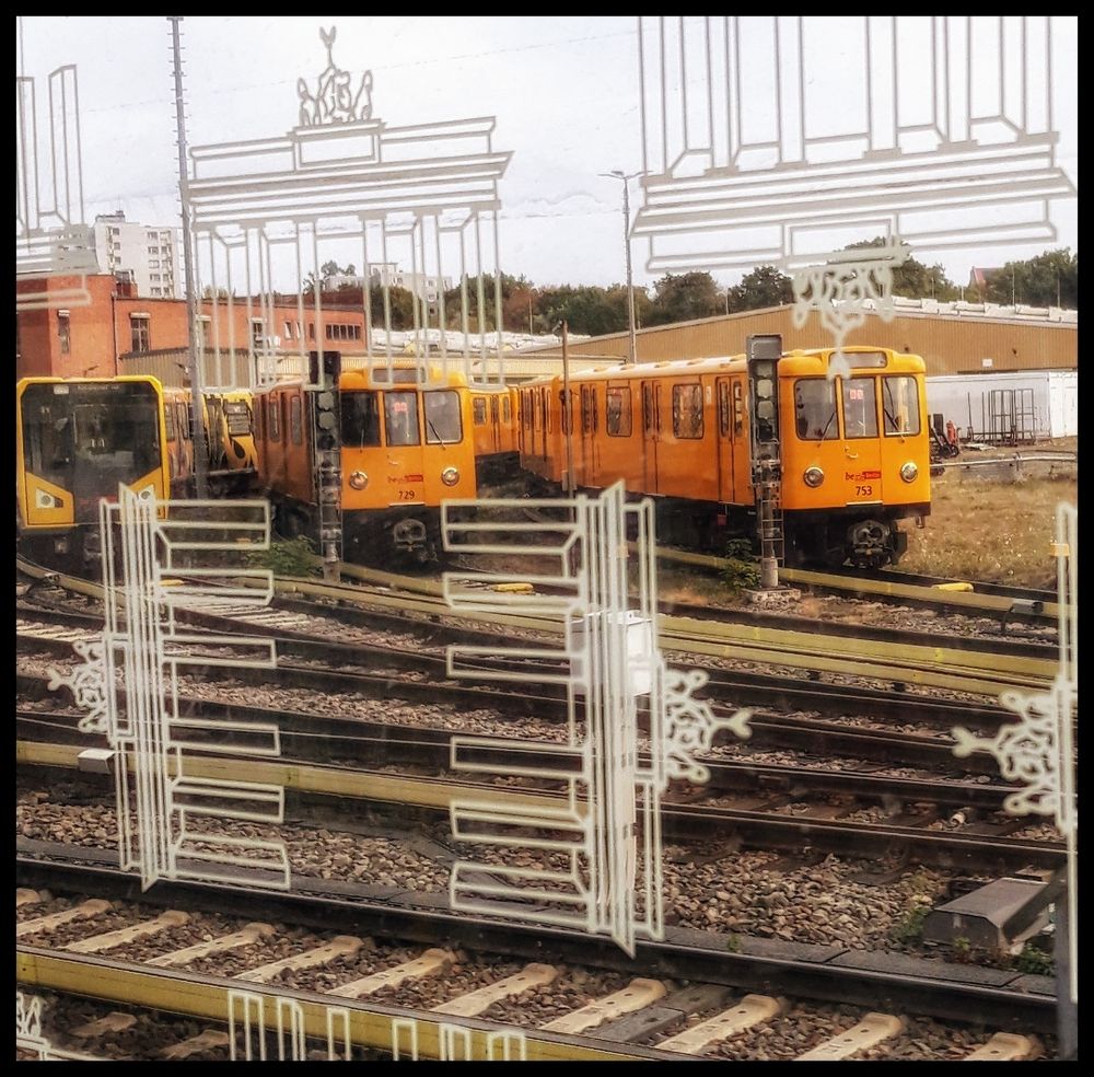 Farbaufnahme aus einer Ubahn durch das Fenster, welches mit vielen halb durchsichtigen Strichzeichnungen des Brandendenburger Tores beklebt sind. Draußen sieht man zahlreiche abgestellte UBahnwagen stehen.