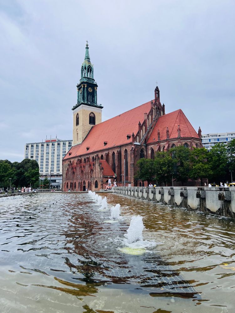 St. Mary's Church in Berlin, near Alexanderplatz. You can see a fountain with water. It’s summer and colorful.