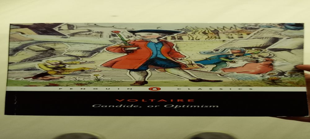 A photo of the cover of Voltaire's Candide, or Optimism. It is a Penguin Classics edition sporting a colorful cover illustration of the main character, Candide, with a background consisting of some of the aweful events he encounters throughout the book. 