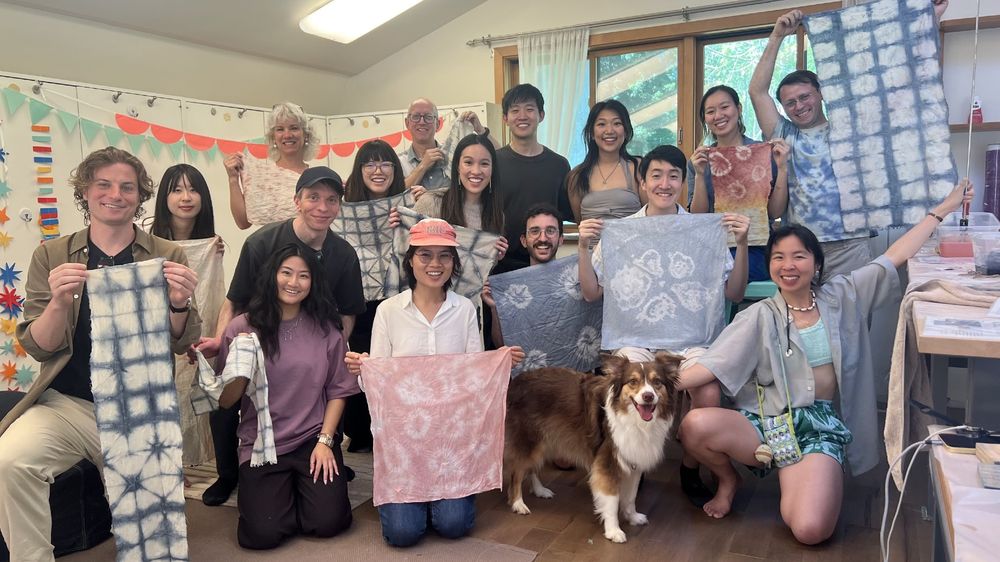 A group of 16 people hold up naturally dyed fabrics of different colors.
