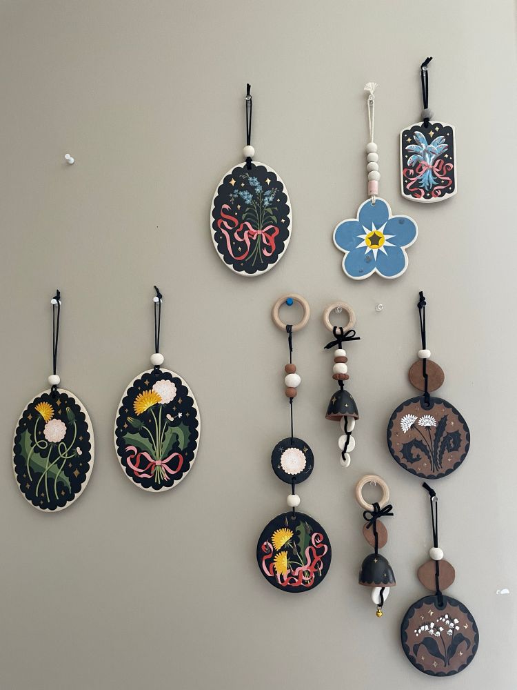 A greige wall with a bunch of ceramic plaques with original paintings by me hanging on it from pushpins. It’s a lot of black and flowers and pink ribbons.