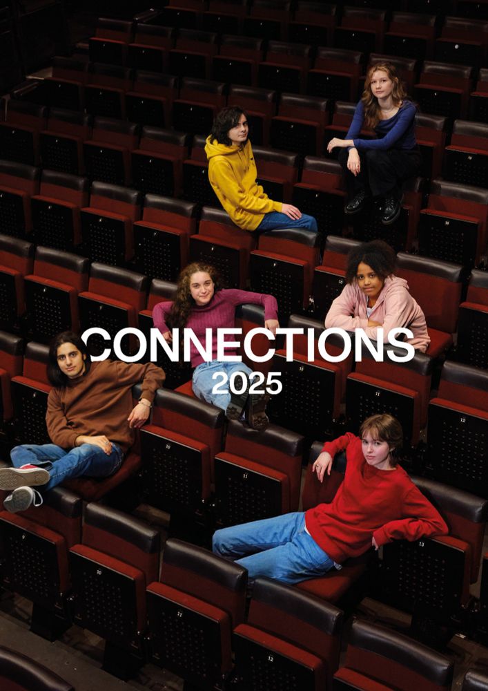A group of six young people are casually lounging in an empty theatre with red and black seats, spread across different rows. They wear colourful, relaxed clothing, including sweaters in shades of red, pink, yellow, and brown, with some leaning on armrests or sitting with legs stretched out. The bold white text overlay reads "CONNECTIONS 2025," suggesting this is promotional material for a theatrical or artistic project.