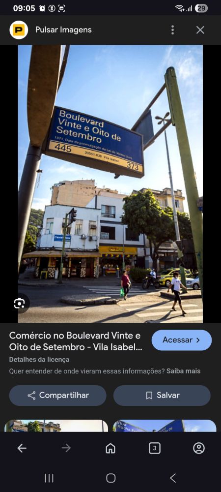 Fotografia de um pedaço da rua 28 de setembro, a frente no alto em um poste a placa com o nome da rua e embaixo lojas, a faixa de pedestres com 02 pessoas atravessando e um taxi parado no sinal. O transito vai da esquerda pra direita
