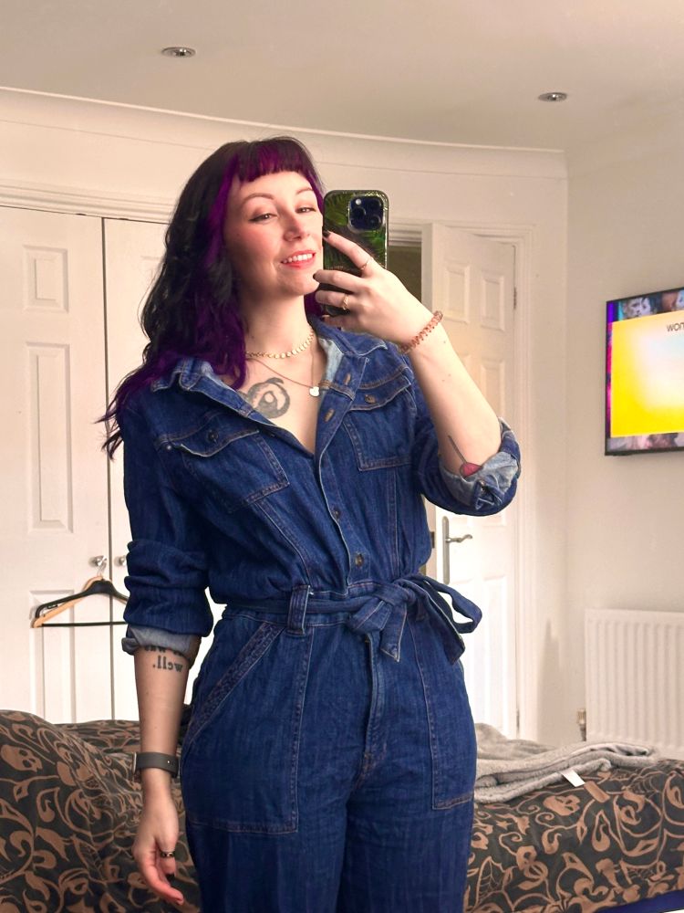 Mirror selfie of mollie. She is wearing a denim jumpsuit. 