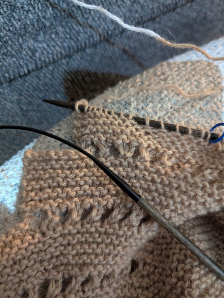 Brownish gray yarn being knit into a shawl with periodic lacing. Still on the needles. 