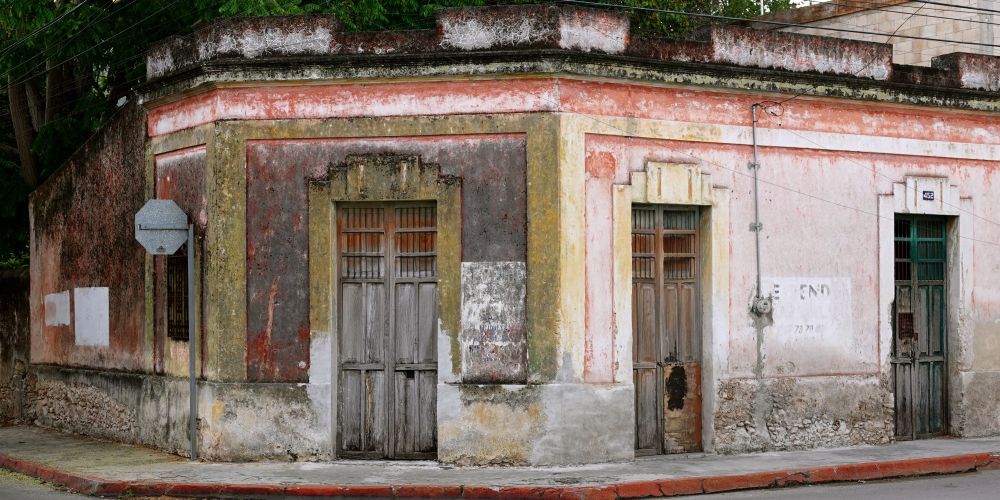Historisches Eckhaus in Mérida mit verwitterter rosa und gelber Fassade, traditionellen Holztüren, ornamentalen Säulendetails und sichtbaren Altersspuren.