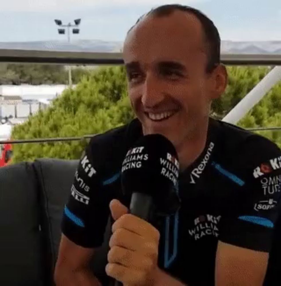 a man wearing a shirt that says williams racing is smiling and holding a microphone