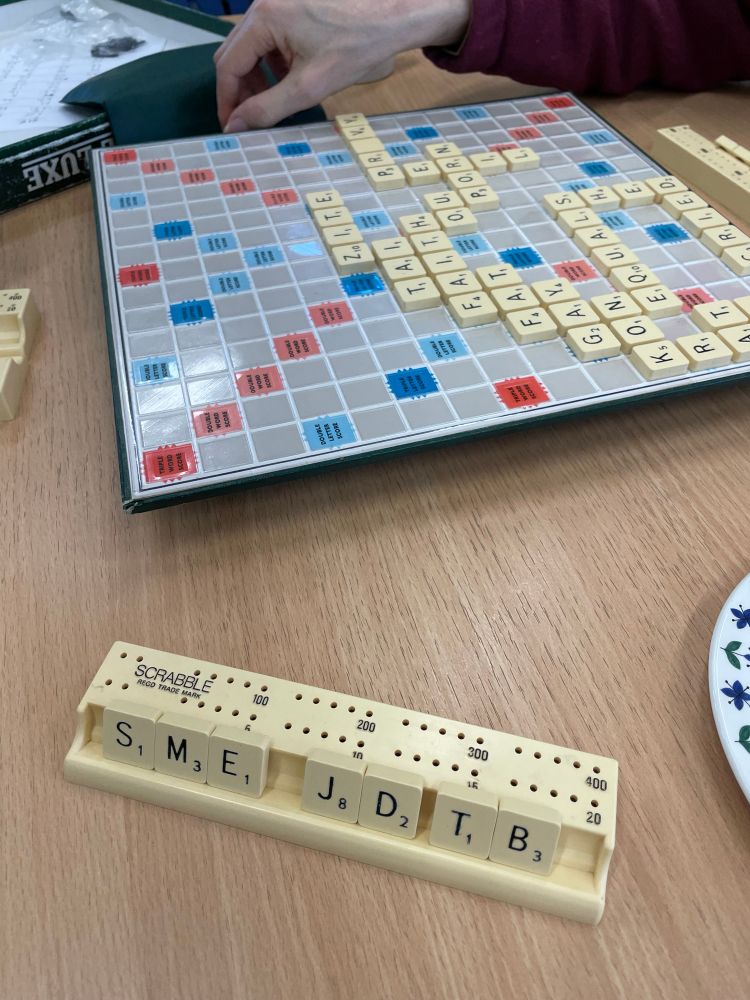 A scrabble board and letter rack with the tiles; S, M, E, J, D, T, B. 