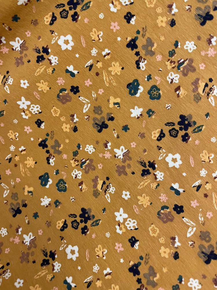 Close up of yellow fabric with a flower print of tiny petals and leaves in white, black, brown, dark green, pink and yellow. On a yellow back ground. It is indeed very yellow. 