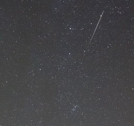 Foto van een stukje sterrenhemel met een heldere meteoor erin. 