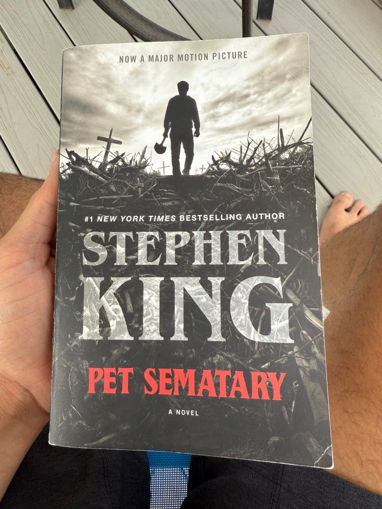 The novel, “Pet Sematary” by Stephen King in the hand of a guy sitting down