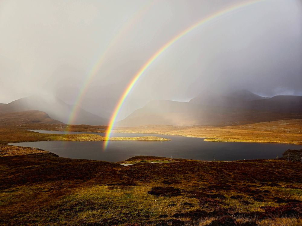 Double rainbow arching up from a lochan over Cul Mor