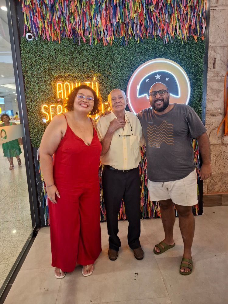 Eu, mulher branca de macacão vermelho; meu avô, homem idoso de camisa amarela e calça preta; Vinícius, homem negro de camiseta cinza e bermuda creme.