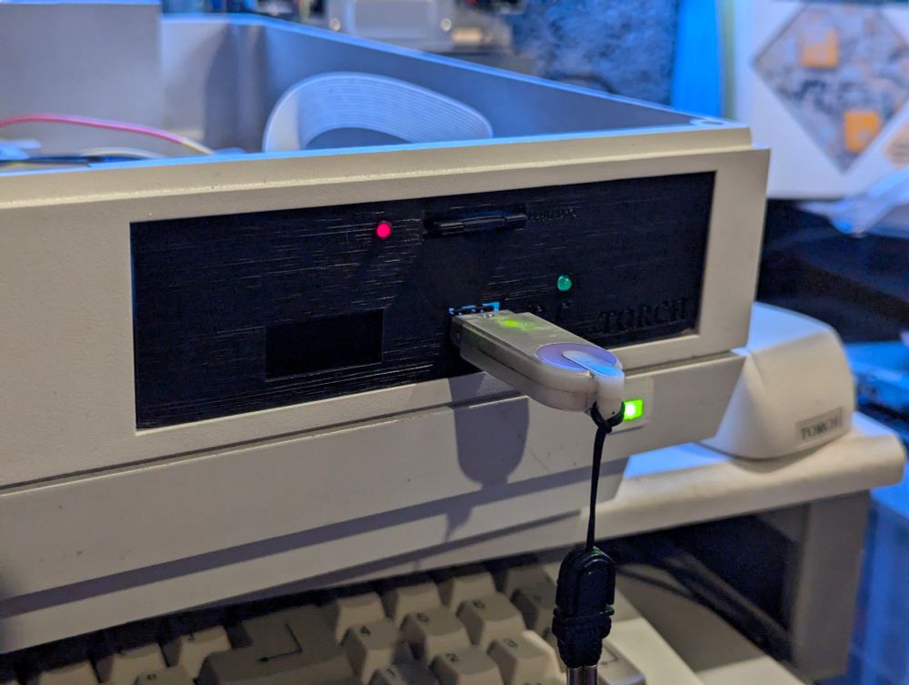 A picture of the latest Gotek bracket installed in the Torch Triple X before the memory problems. There is a silver USB memory stick inserted into the Gotek. An SD card is inserted in a slot at the top and a red LED is lit, indicating that the BlueSCSI is accessing the card.