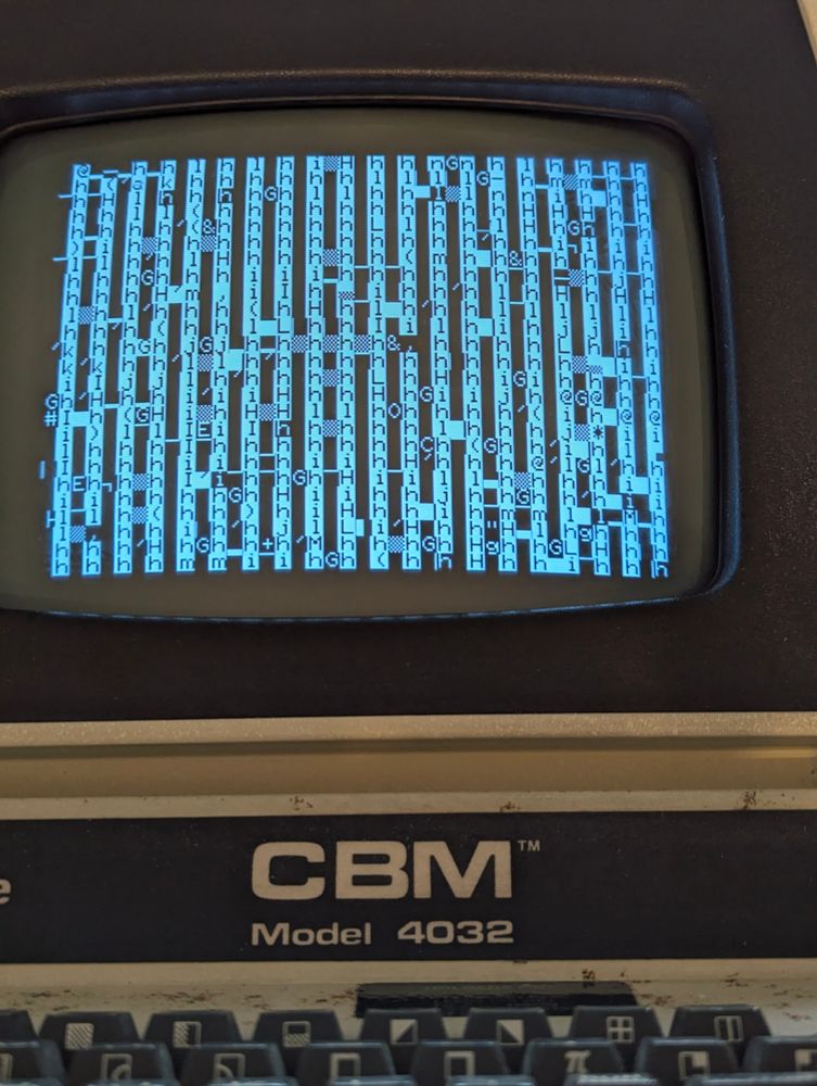 A picture of a Commodore PET 4032 screen. The screen is showing random white vertical stripes, peppered with random symbols, letters and numbers.