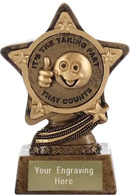 Participation trophy for kids taken from a Google search. It’s a gold star with smaller gold stars on each point. In the middle hasa smiling face emoji with a thumbs up next to it. “It’s the taking part that counts” is the text surrounding the smiling face. The bottom has a brass plate that says, “Your engraving here”