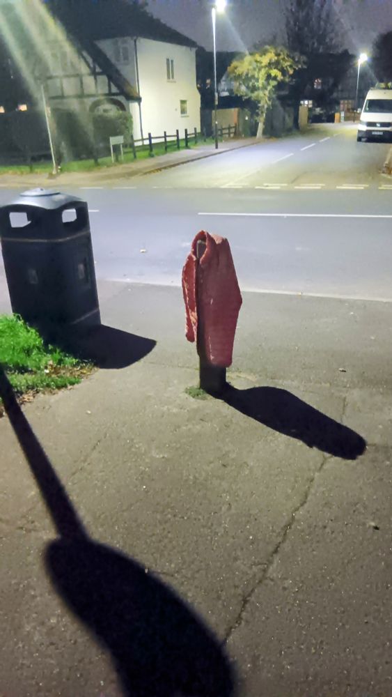 A wooden bollard draped in a child's red coat, looking like the demonic girl in 'Don't Look Now'. 