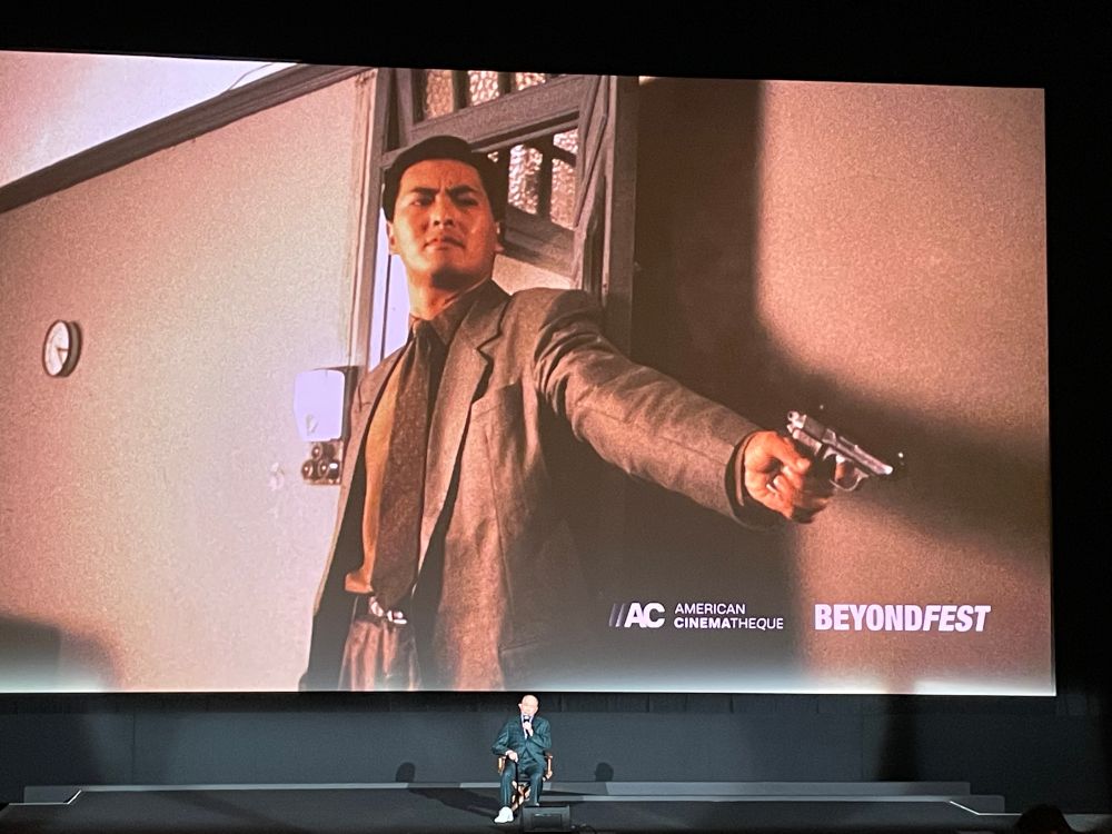 JOHN WOO sitting beneath a movie screen with Chow Yung Fat in THE KILLER