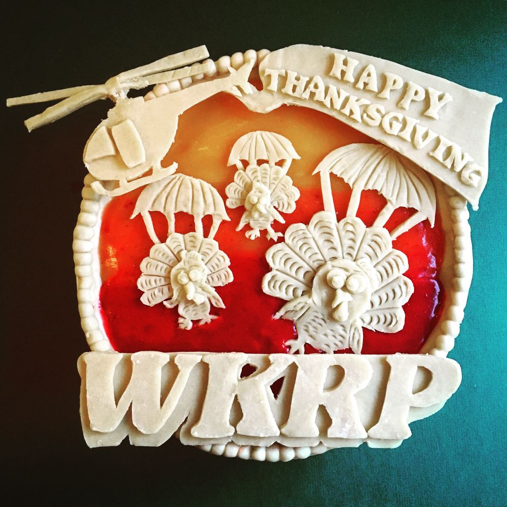 A pie with the letters, WKRP from the television show of the 1980s. Also decorated with turkeys with parachutes jumping from a helicopter that has a happy Thanksgiving banner trailing behind.