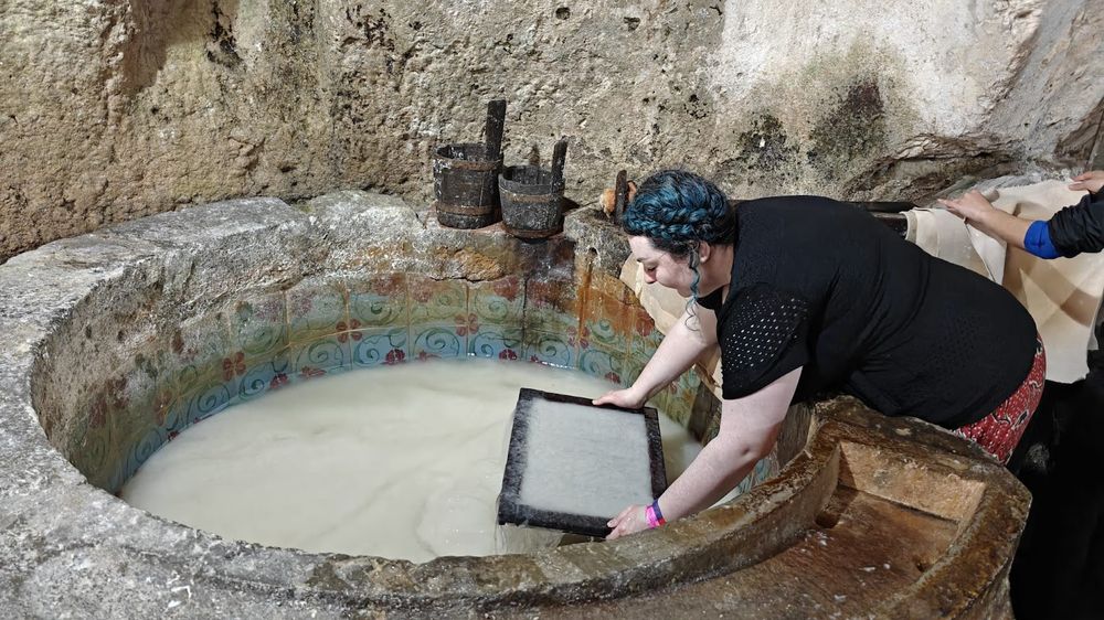 Isla leaning over a large well filled with cotton rags, filling a frame with pulp to make traditional paper, at the Museo della Carta in Amalfi.