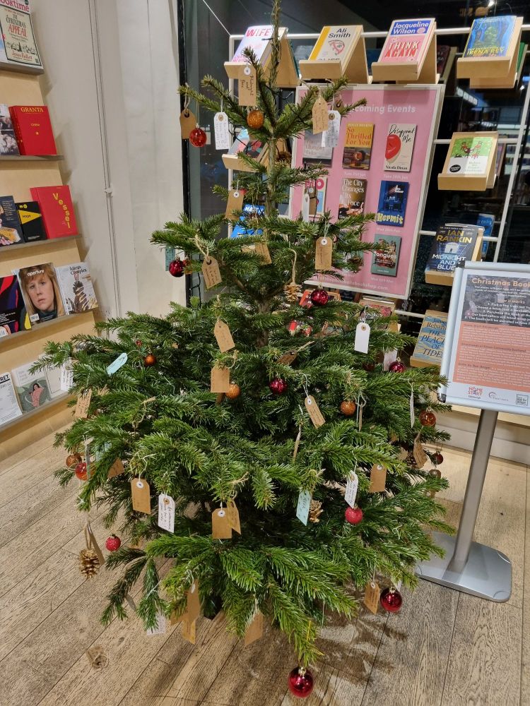 A christmas tree in a bookshop with lots of labels hanging from it. 