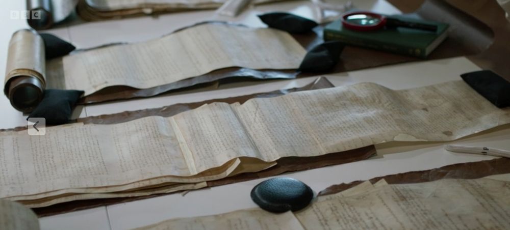 smooth black stone, a paper weight, on an old scroll, three scrolls side by side, like old screens, full of information.