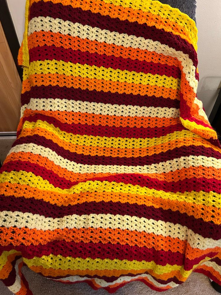 A crochet blanket with stripes of reds/yellows/oranges