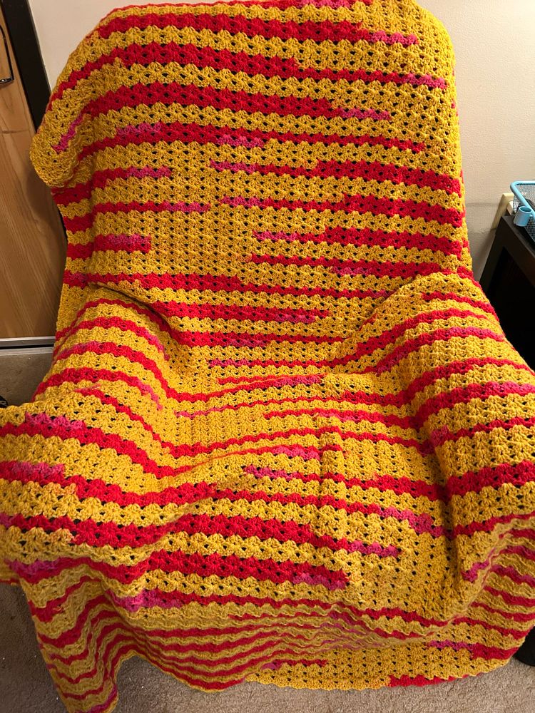 A crochet golden blanket with small stripes of red and pink