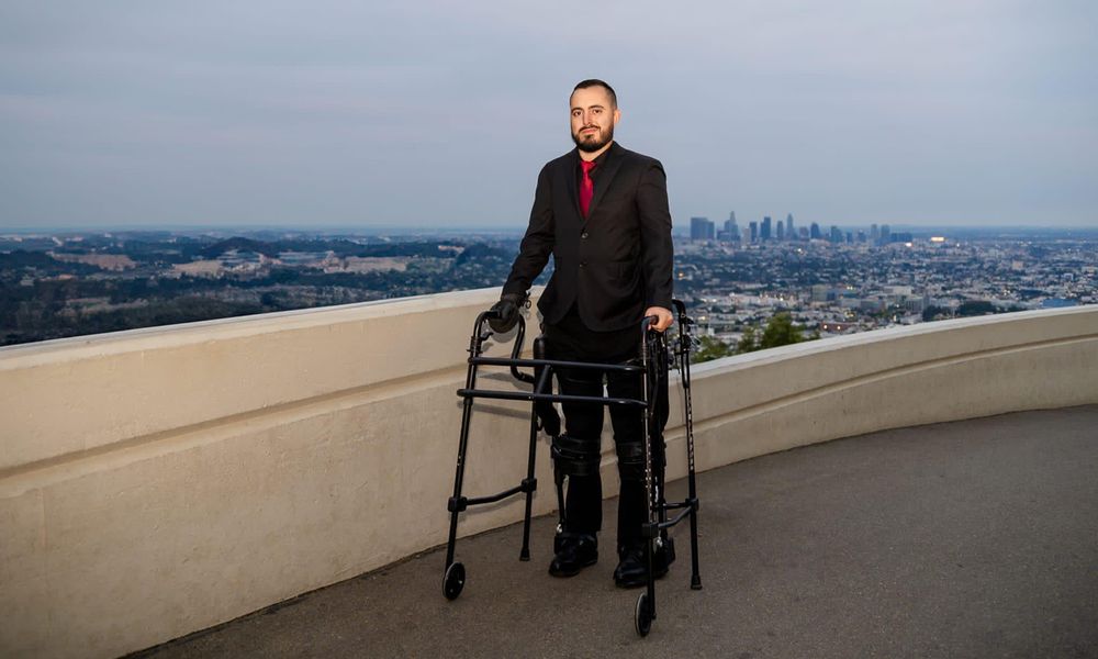 Ignacio Montoya stands with a walker in front of the Los Angeles skyline.