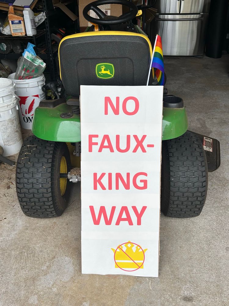 Protest sign leaning against a riding lawnmower. Sigh says NonFaux-King Way 