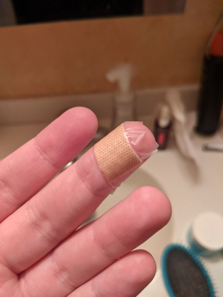 A photo of my left hand in my bathroom. There is a bandage wrapped around my middle finger, so as to stop bleeding from a cut. 