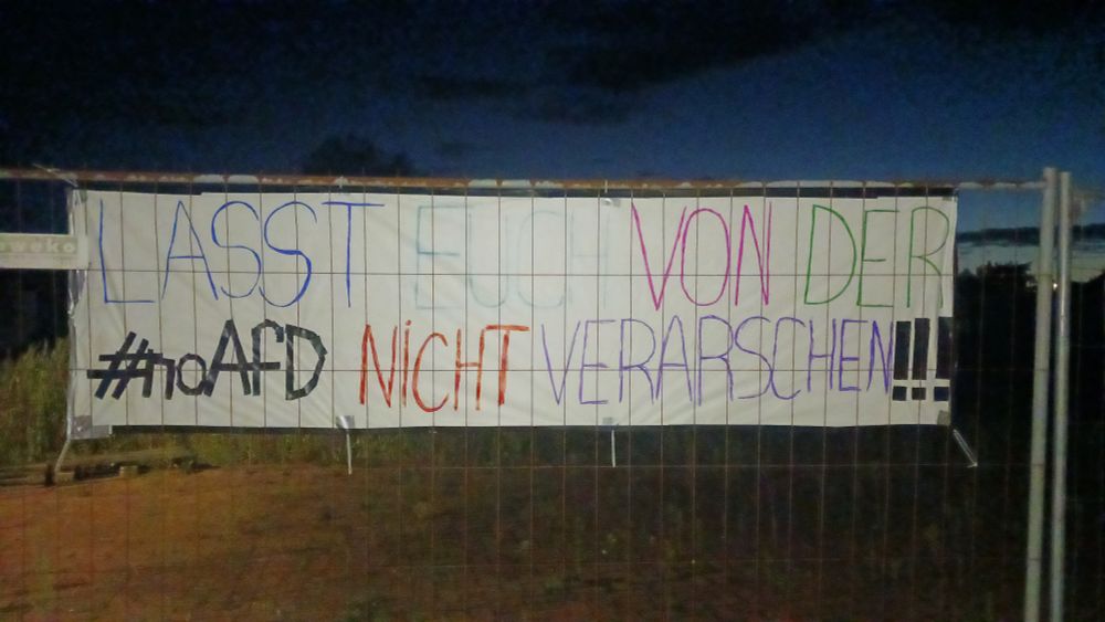 Banner an Bauzaun mit bunter Schrift: "Lasst euch von der #noAfD nicht verarschen!!!"