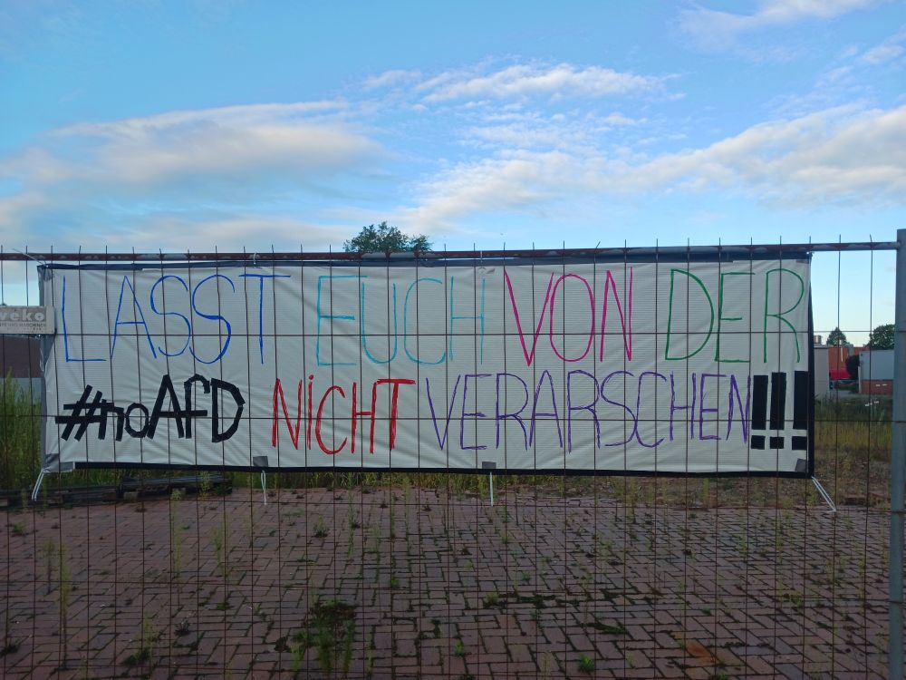 "Lasst euch von der #noAfD nicht verarschen!!!" steht bunt auf einem Banner an einem Bauzaun.