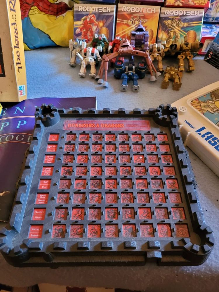 An electric Dungeons & Dragons game from the 1980s. It looks like a grey, square castle or fortress and the board is a grid of red images that if I recall correctly, would light up as you played the game. 